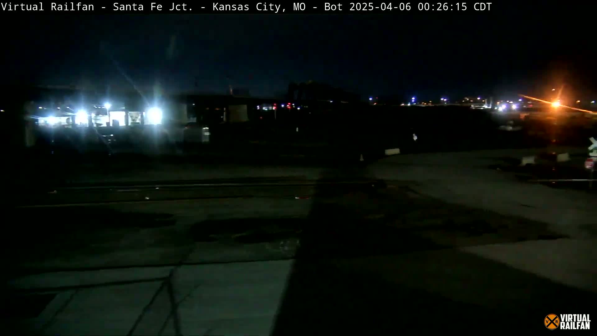 A nighttime view of a dimly lit rail yard with a building and train tracks.