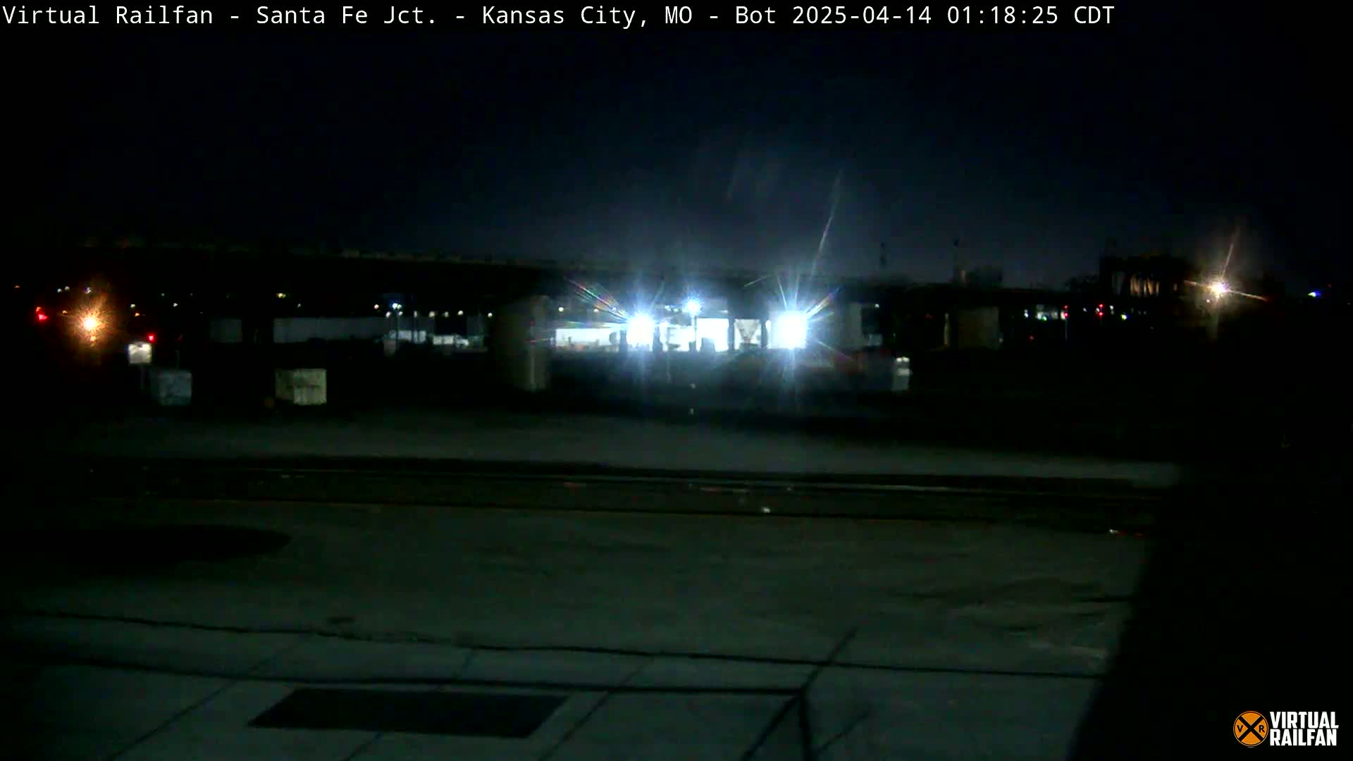 At night, a brightly lit train sits under a bridge in a dark, empty area.