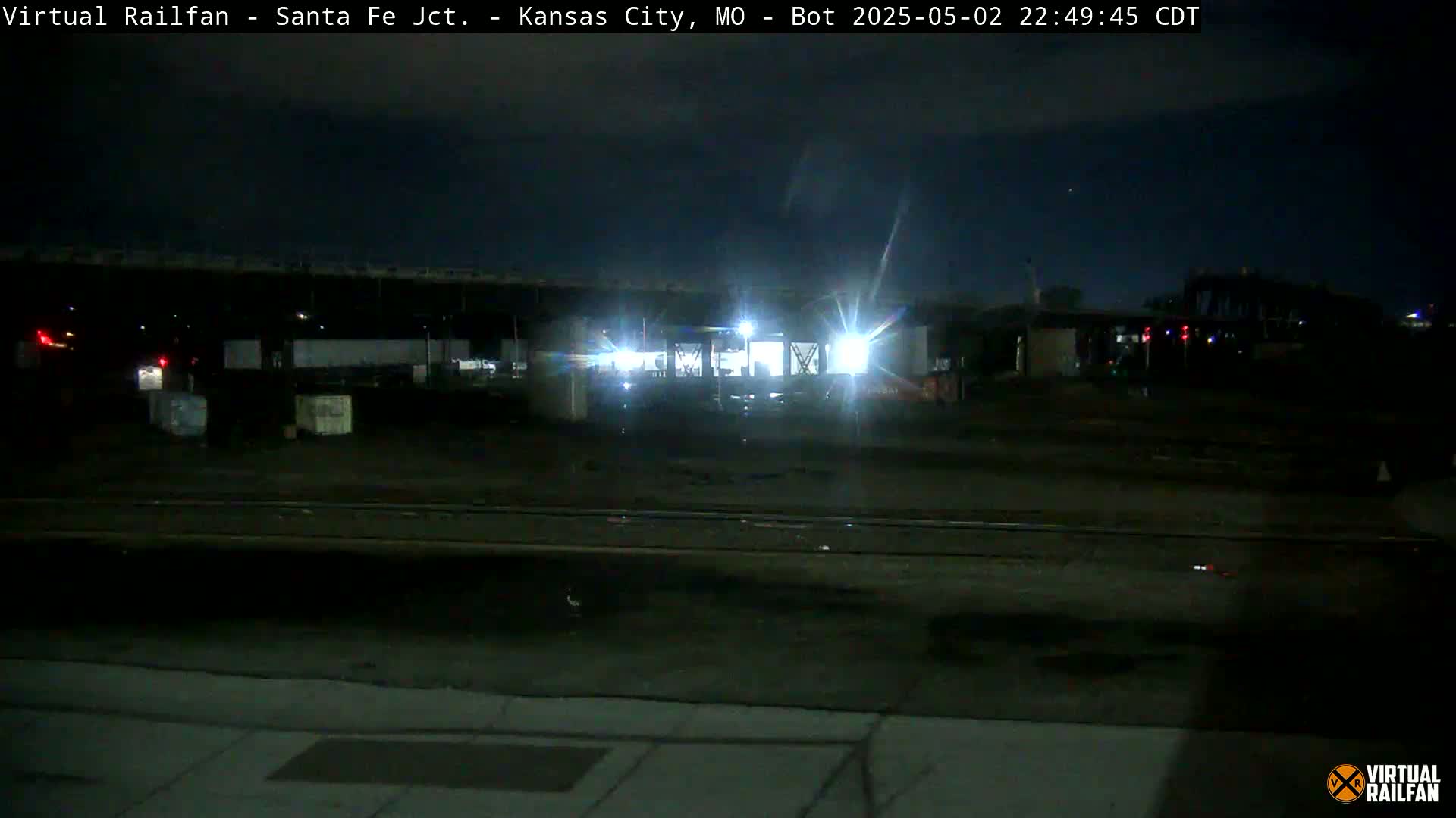A brightly lit train sits on railroad tracks at night under a dark sky.