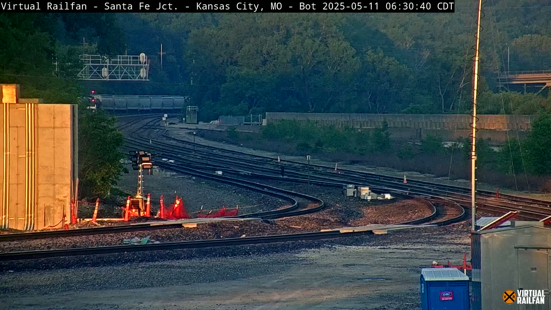 A long freight train is seen passing through a rail yard at sunrise, with several sets of tracks curving around a construction area.