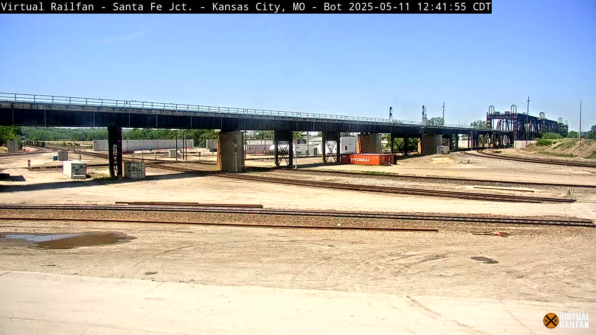 A railway yard with multiple tracks under a bridge on a sunny day.