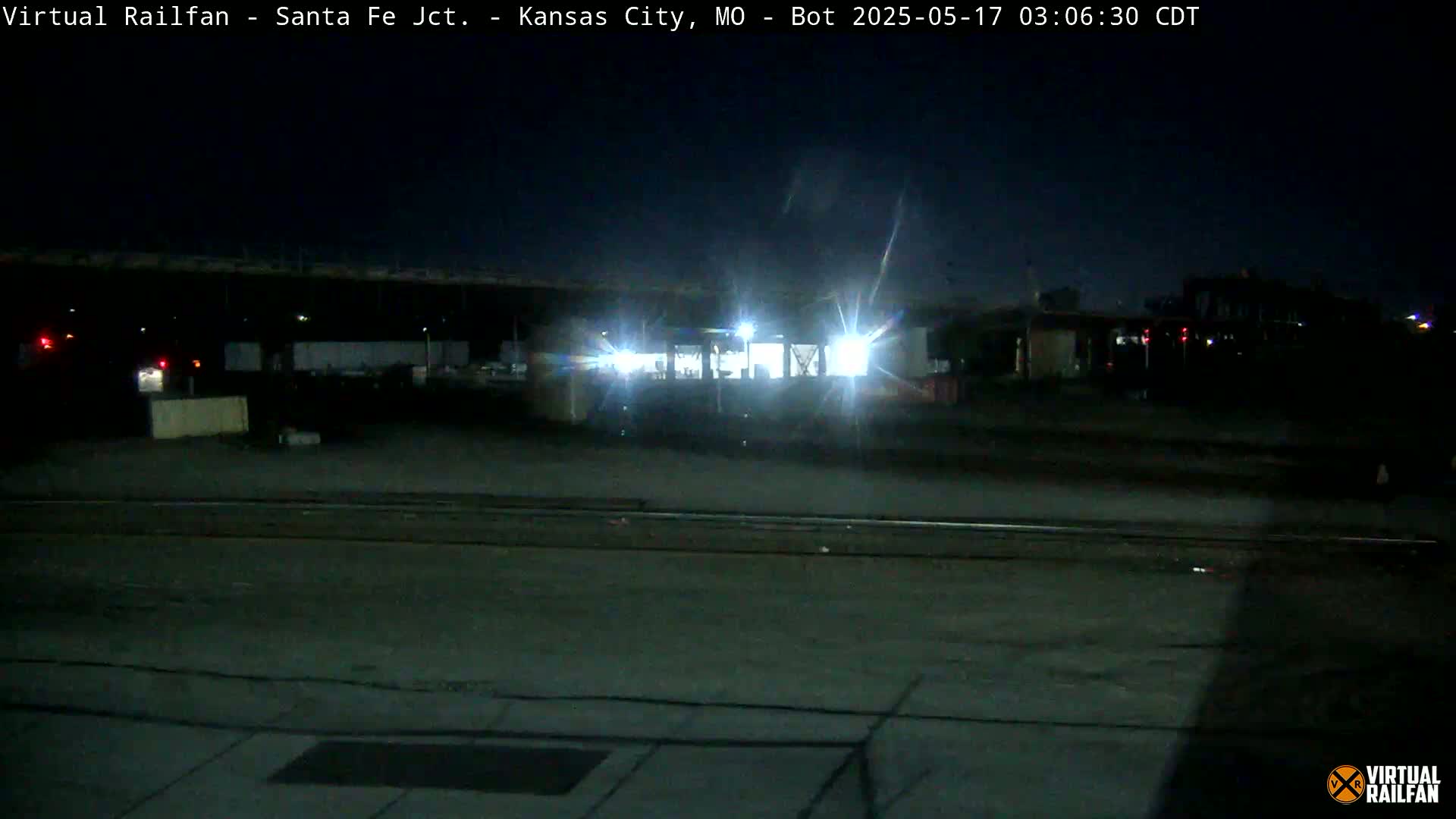 A nighttime view of a train illuminated by its headlights, situated in a rail yard.