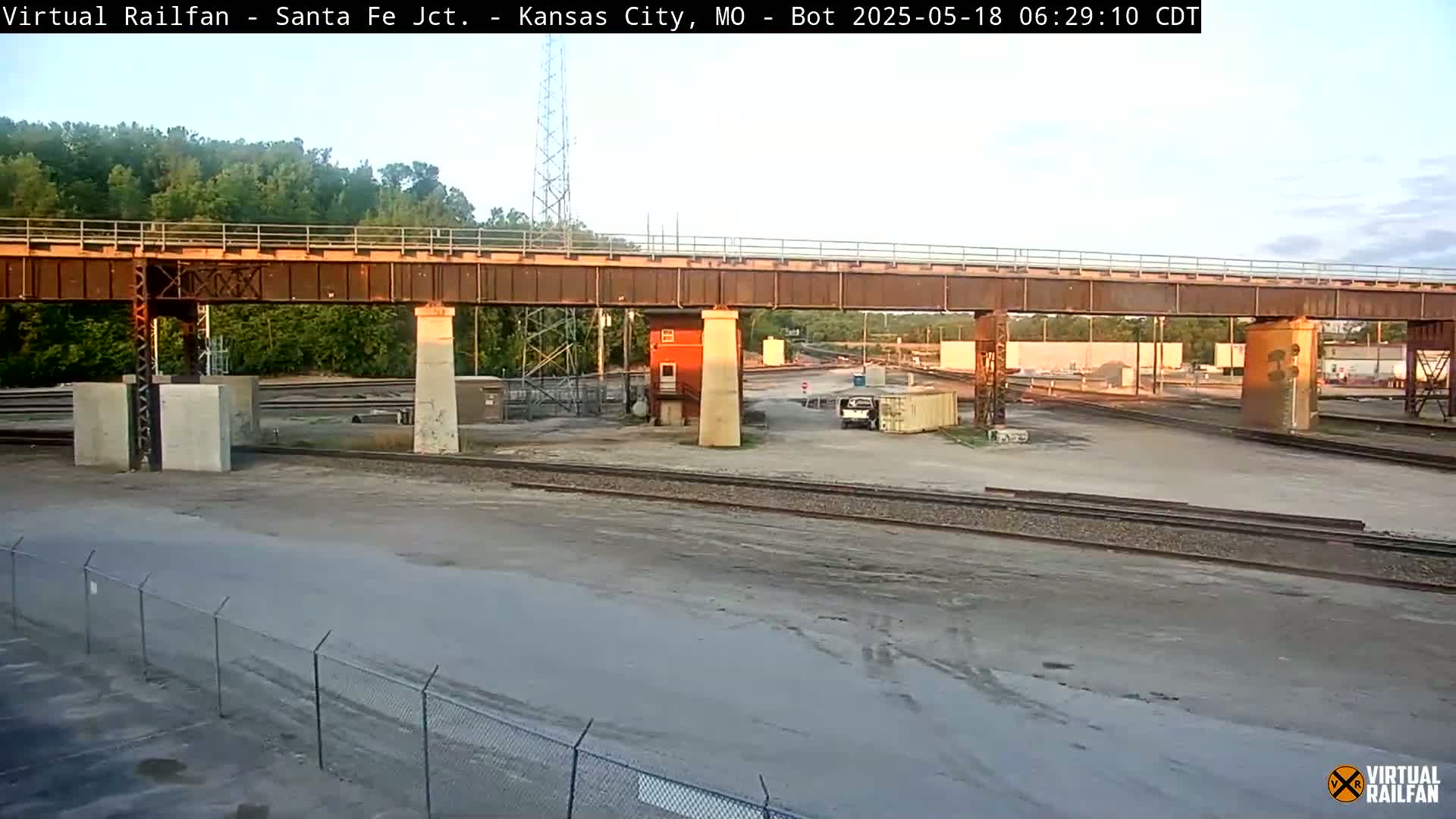 A railway yard with a rusty overpass under a partly cloudy sky.
