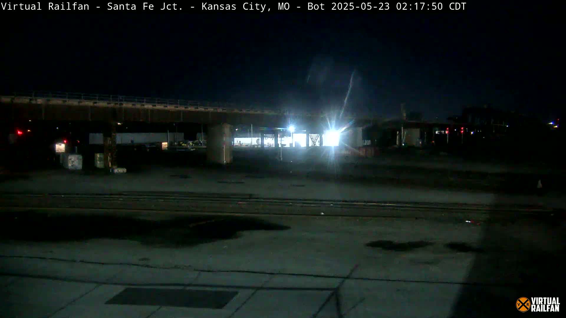 A nighttime view of a dimly lit railroad yard under a bridge.