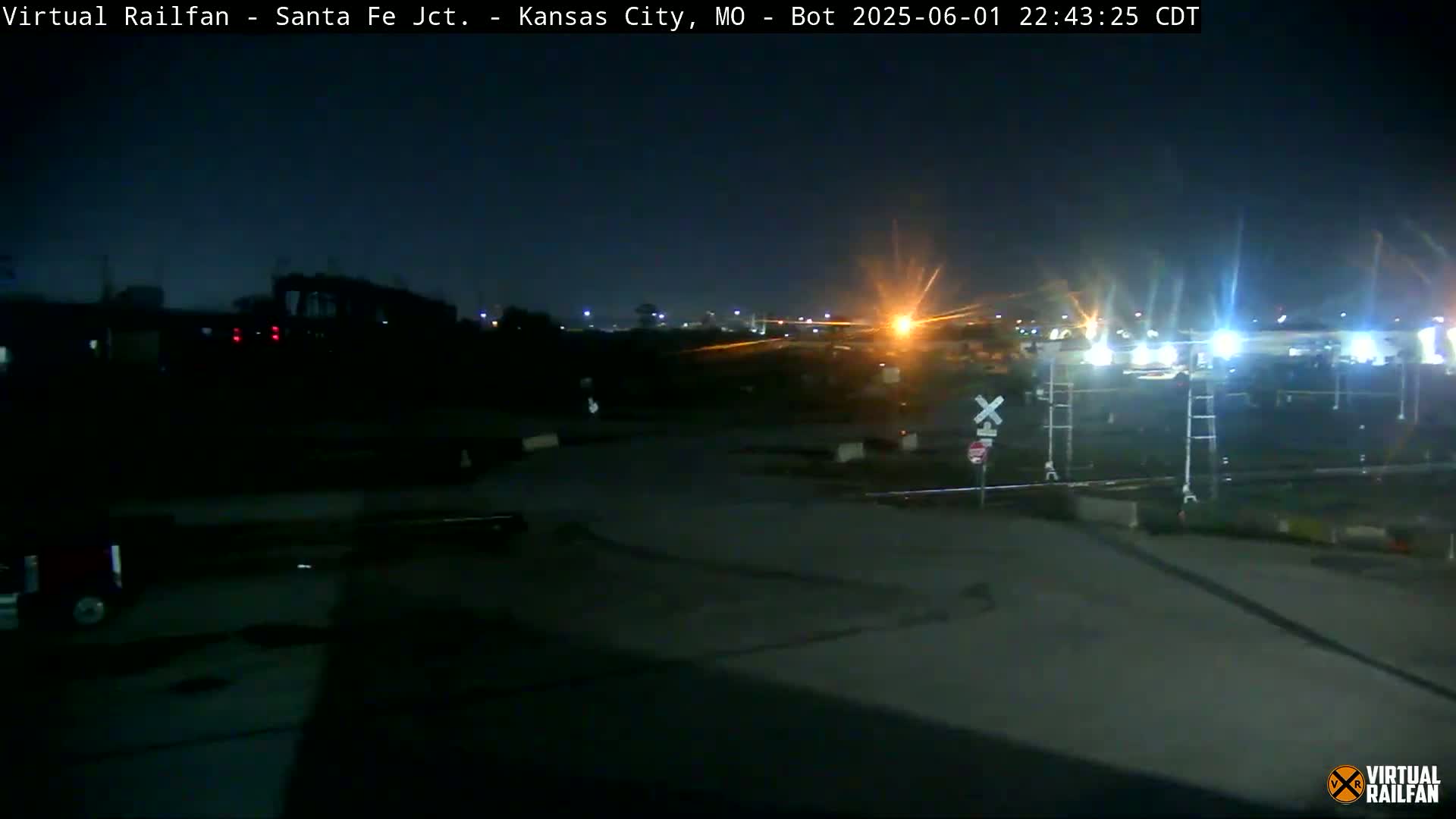 A nighttime view of a dimly lit train yard with railroad crossings and some distant lights.