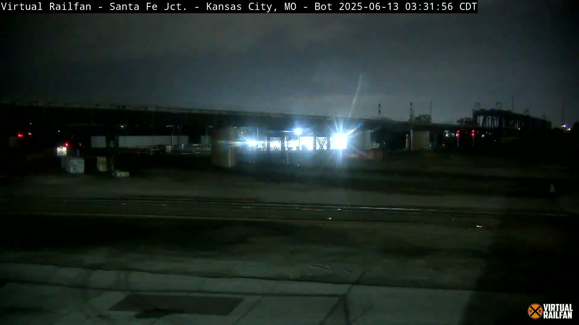 A nighttime view of a dimly lit train yard under an overcast sky.