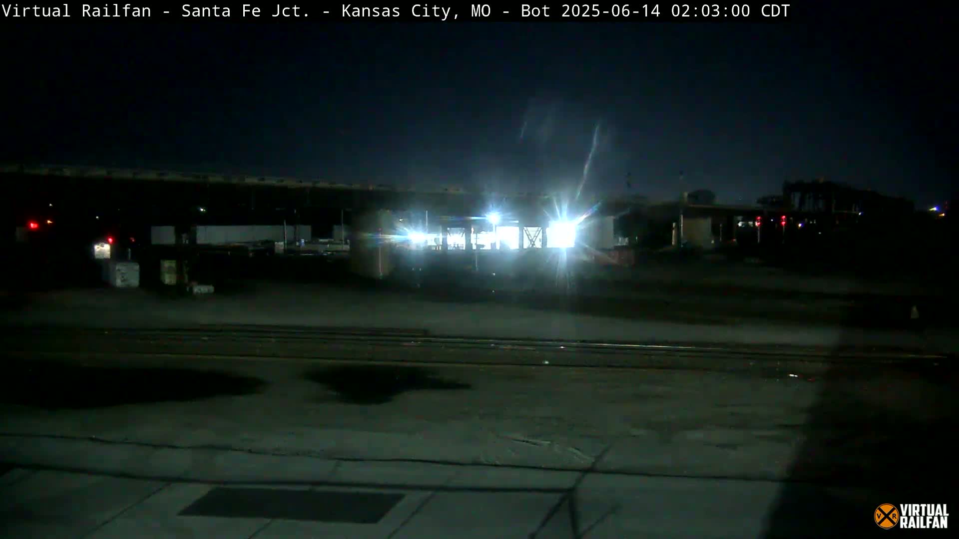 A brightly lit train sits on railroad tracks at night.
