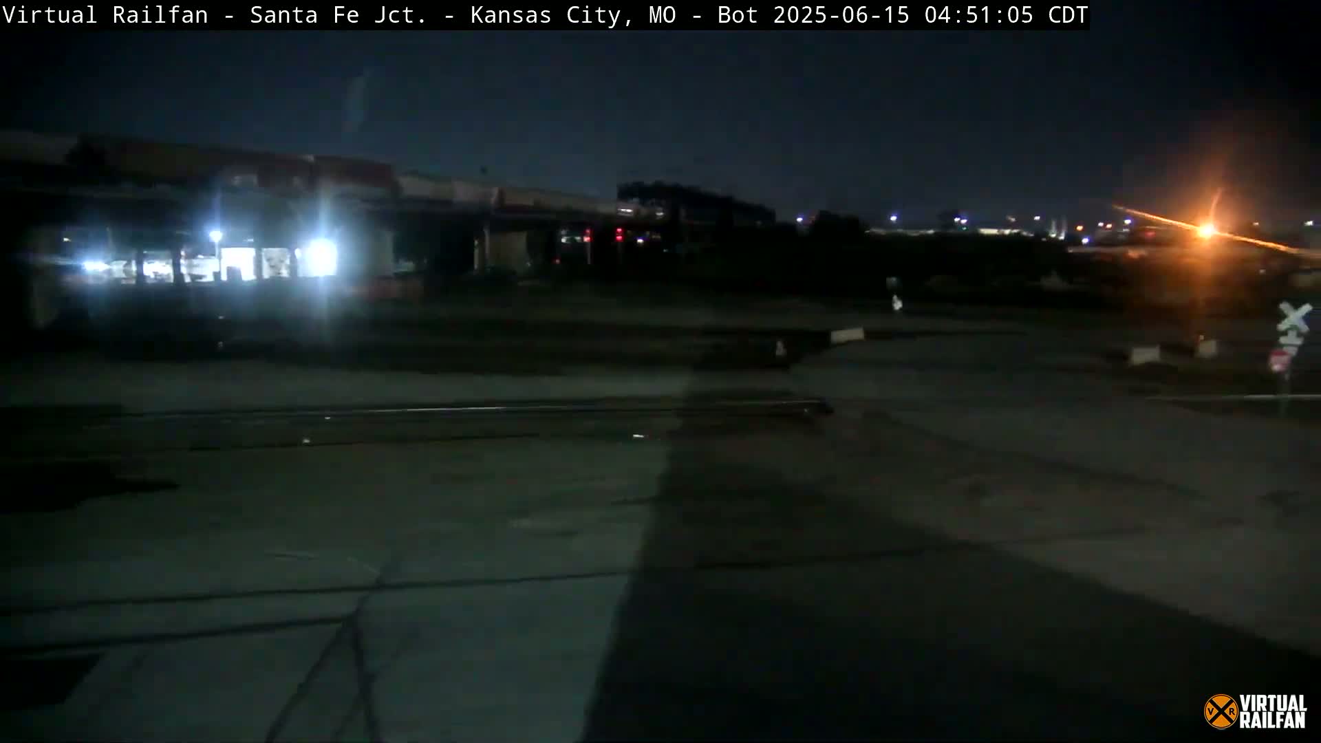 At night, a train is partially visible near railroad tracks in a dimly lit area.