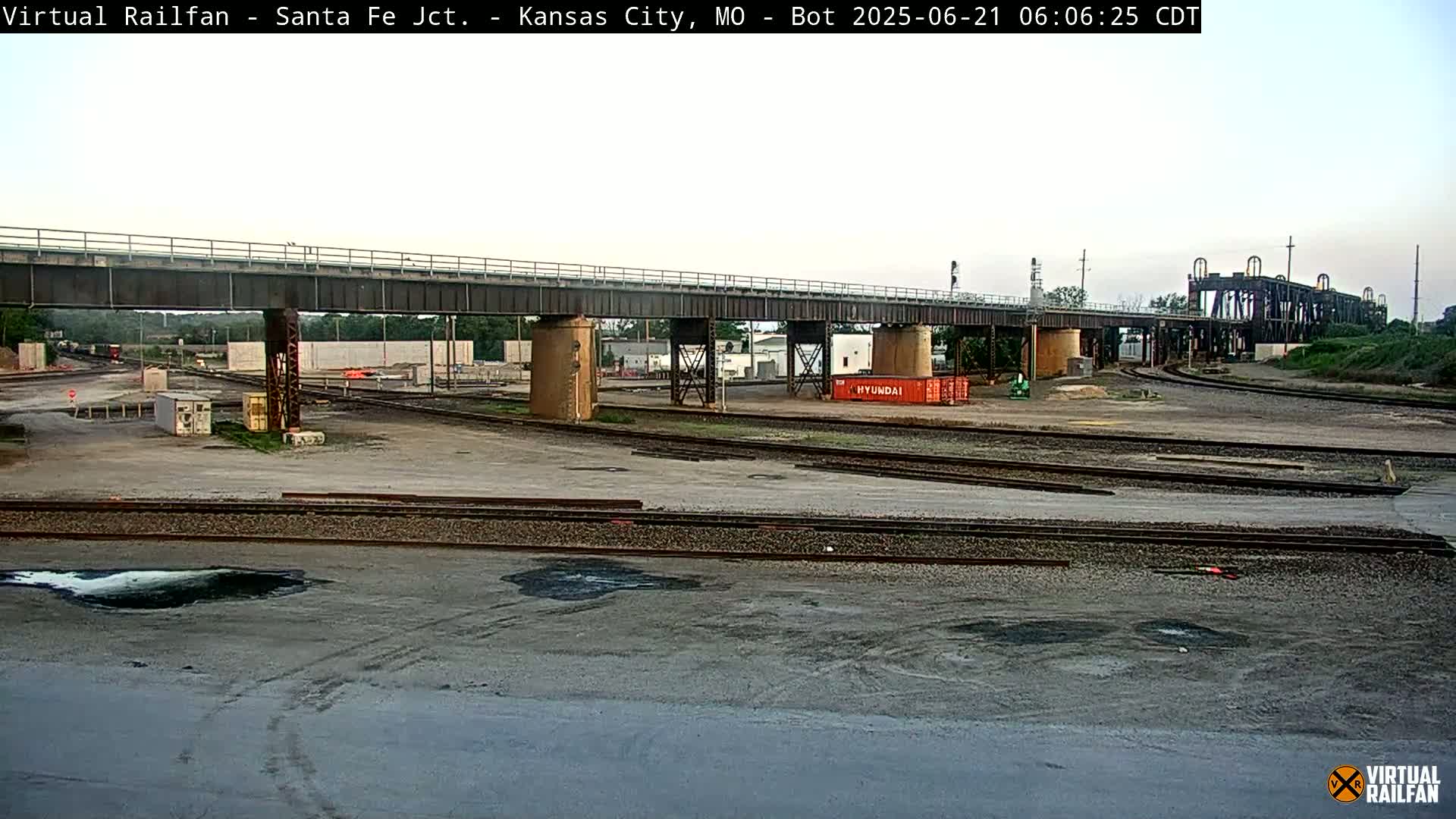 A railway yard with multiple tracks and a large bridge under an overcast sky.