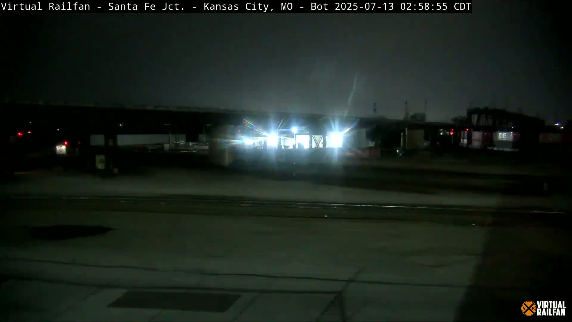 A brightly lit train sits under a dark, nighttime sky in a dimly lit yard.