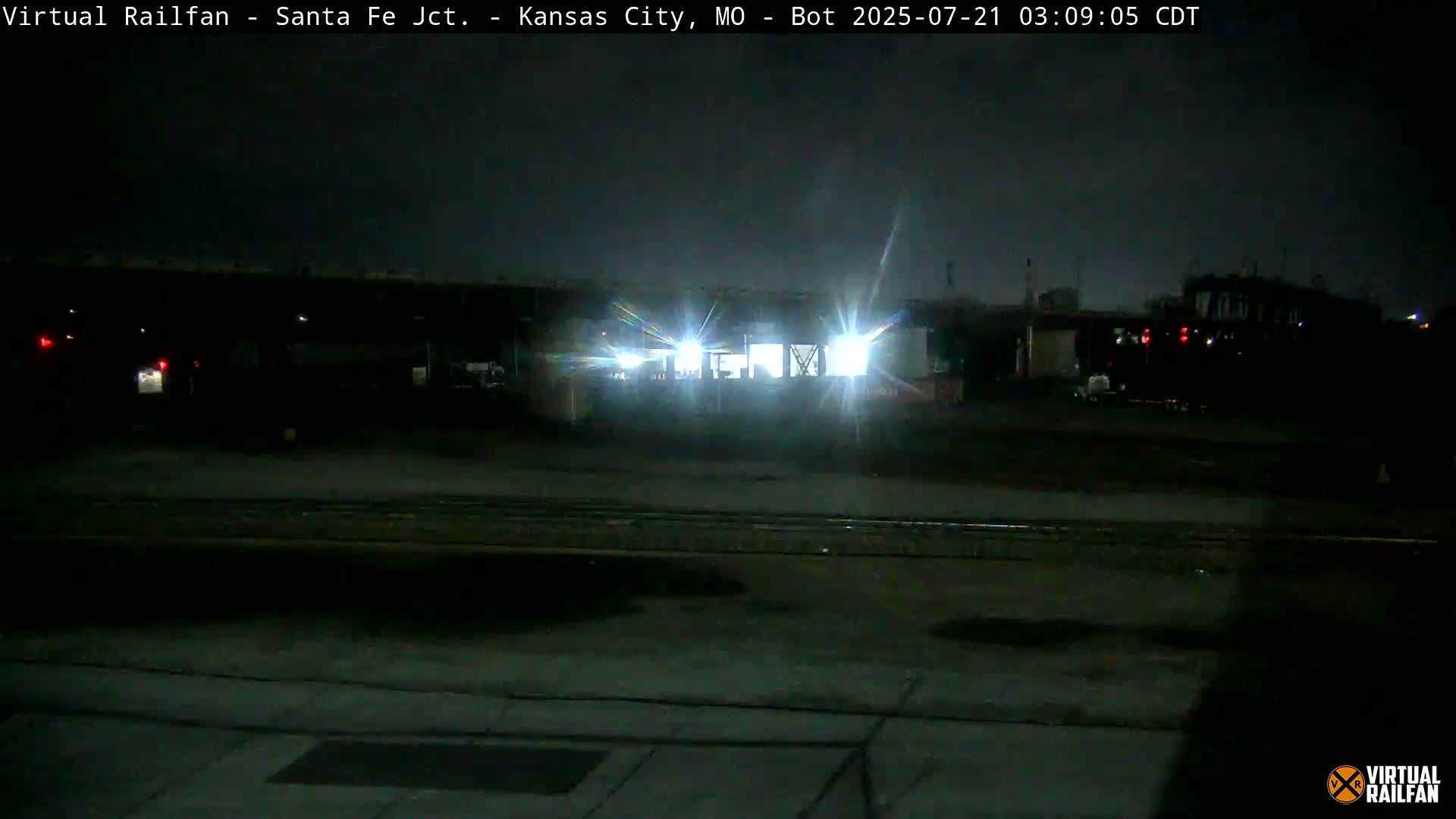 At night, a brightly lit train is visible in a rail yard.