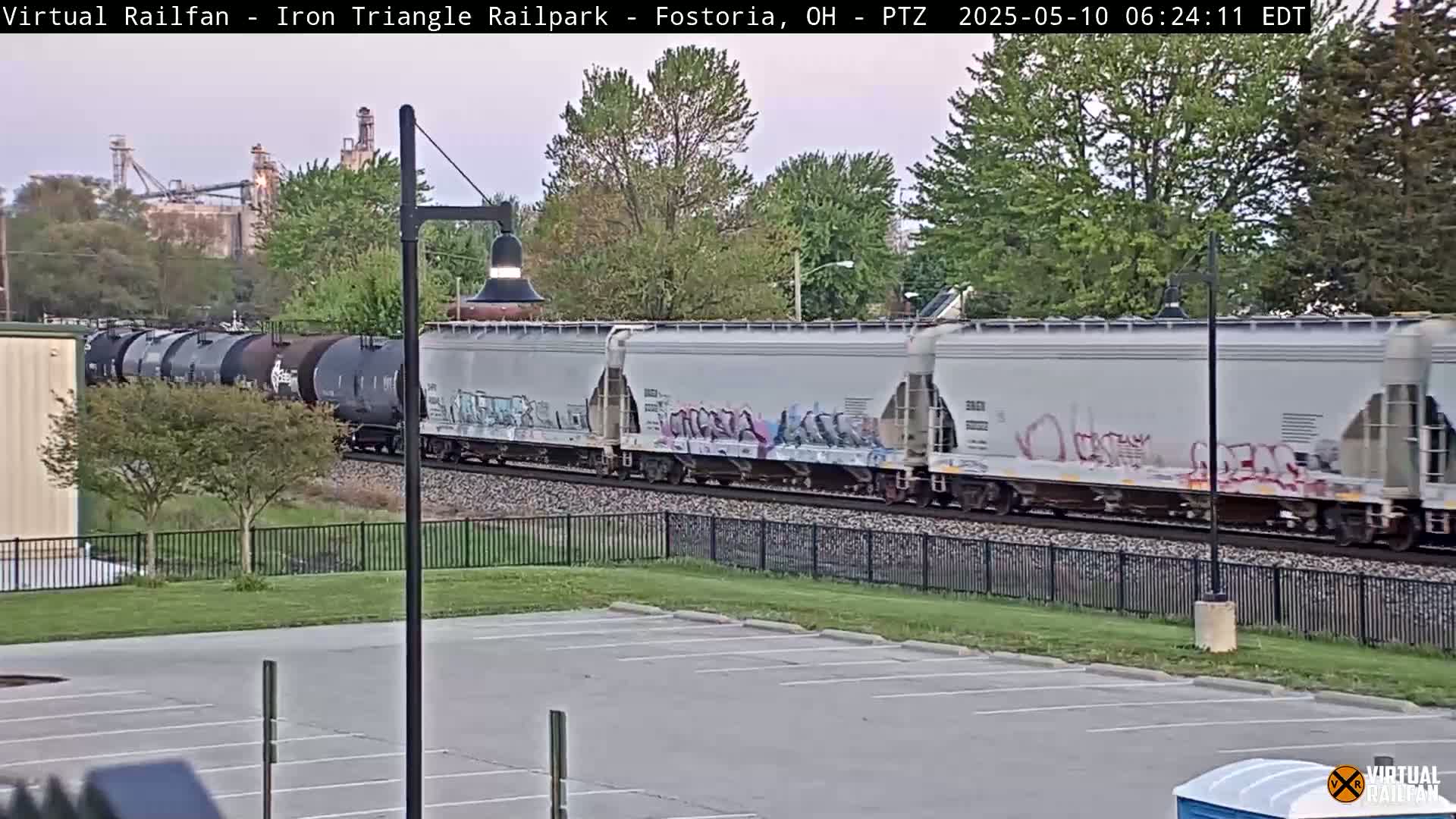 A freight train with graffiti-covered cars passes by a parking lot on an overcast day.