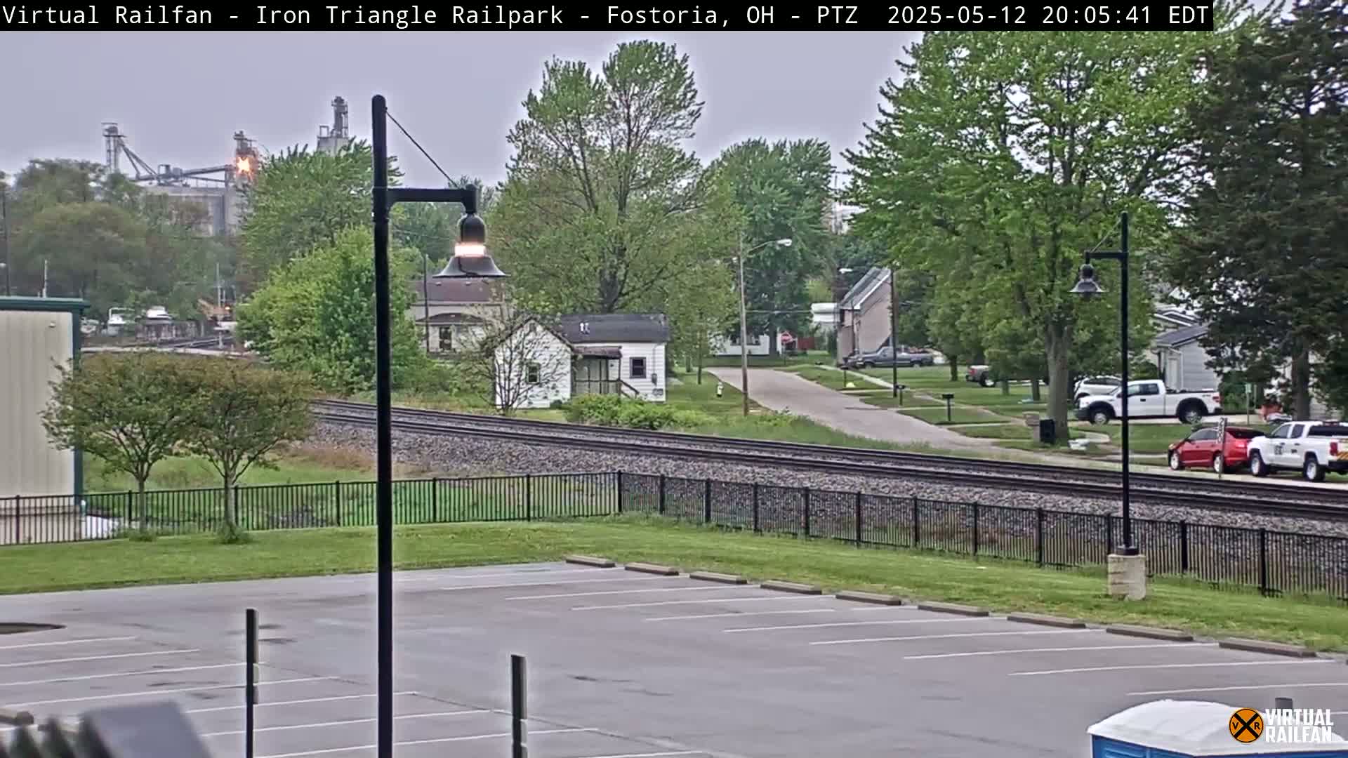 A view of railroad tracks, a parking lot, and residential buildings under an overcast sky.
