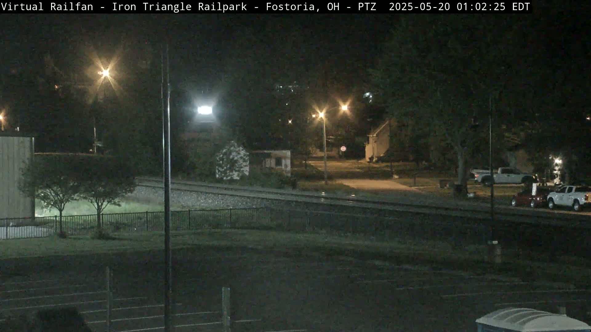 A nighttime view of a railroad crossing near a residential area, illuminated by streetlights.