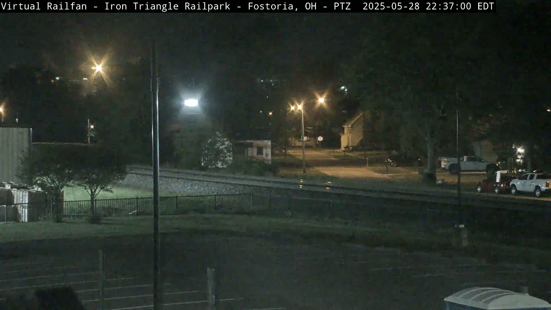 A nighttime view of a rail yard and residential street, illuminated by streetlights.