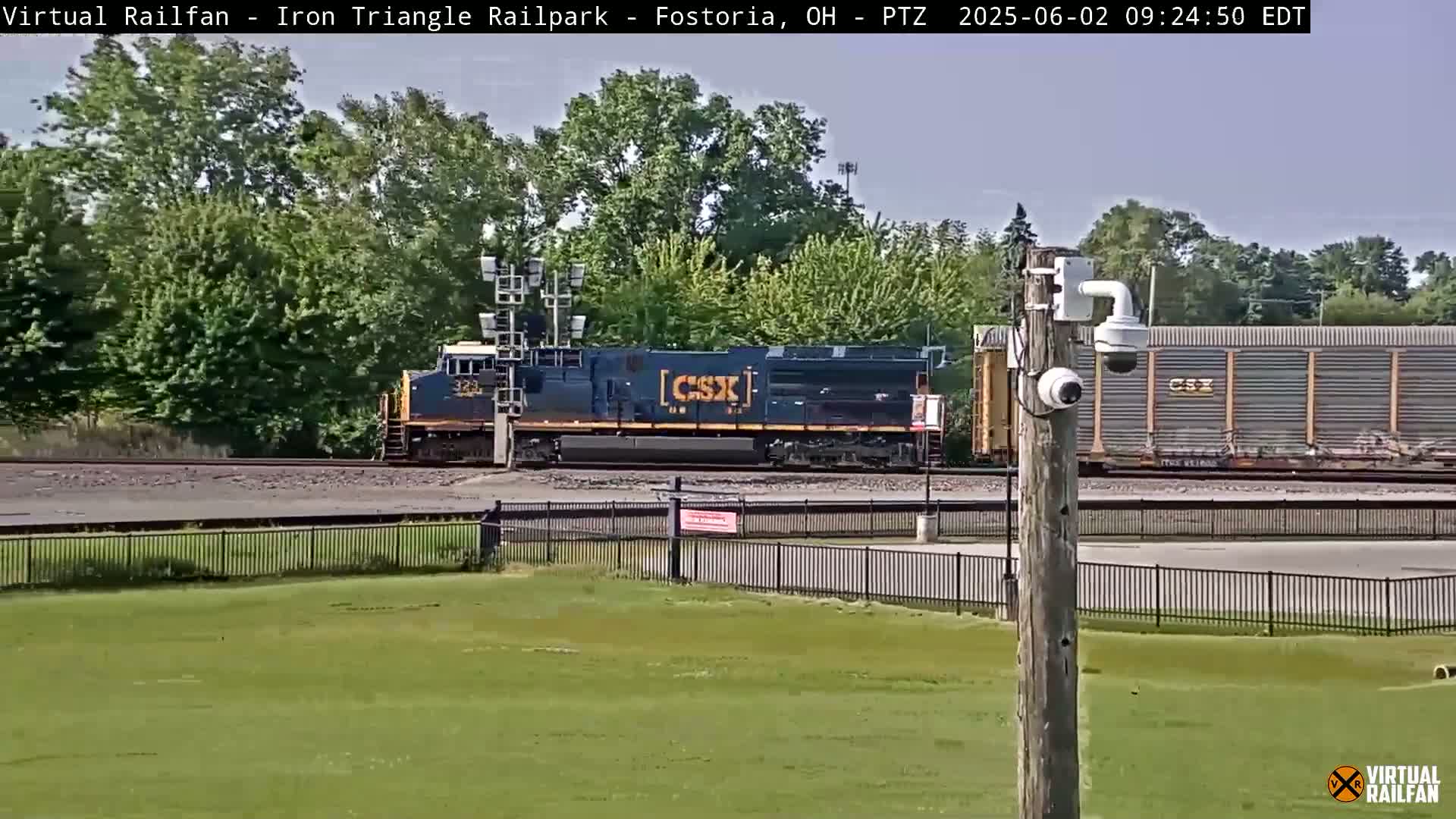 A CSX locomotive and freight cars pass by a grassy area on a sunny day.