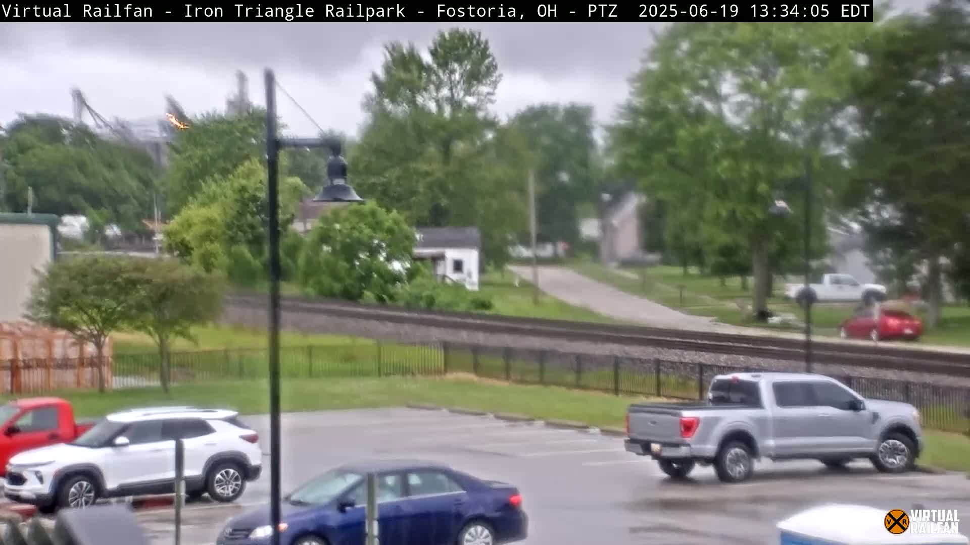 A parking lot with several cars and a pickup truck is seen next to a railway under an overcast sky.