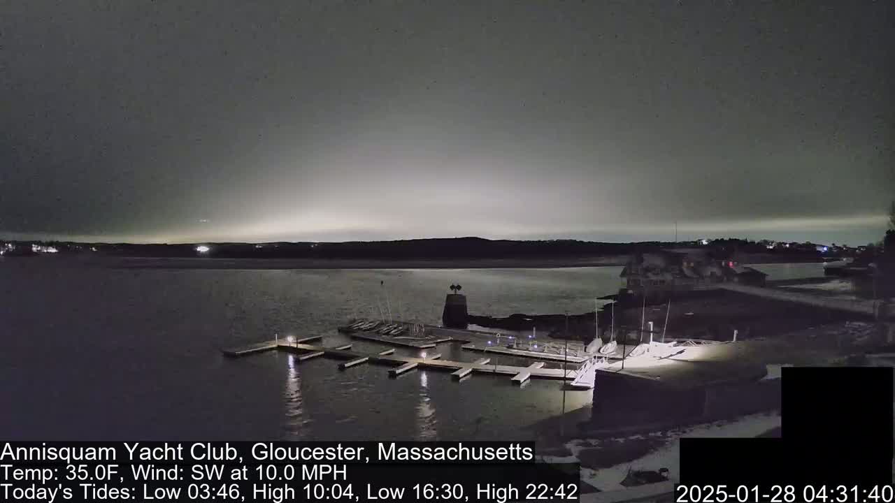 A nighttime view of a marina with boats docked, under a dark, cloudy sky with a faint glow on the horizon.