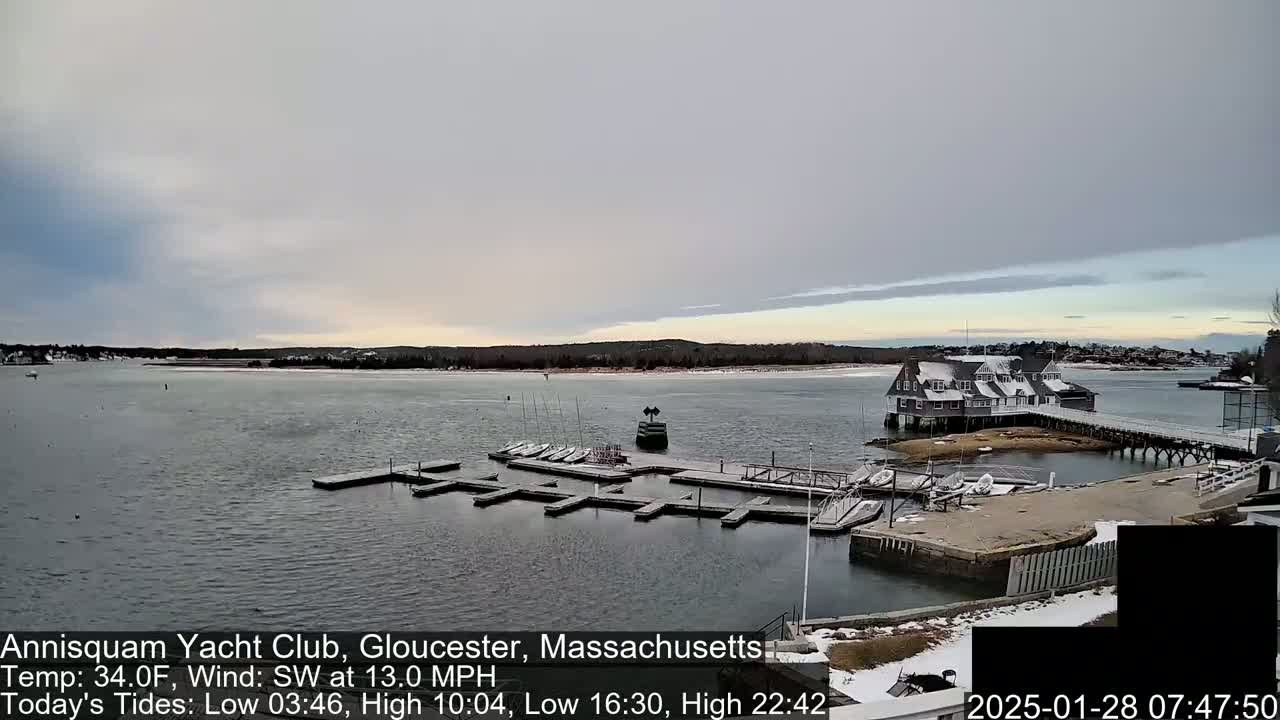 A snow-dusted yacht club sits on a small island in a calm bay under an overcast sky.