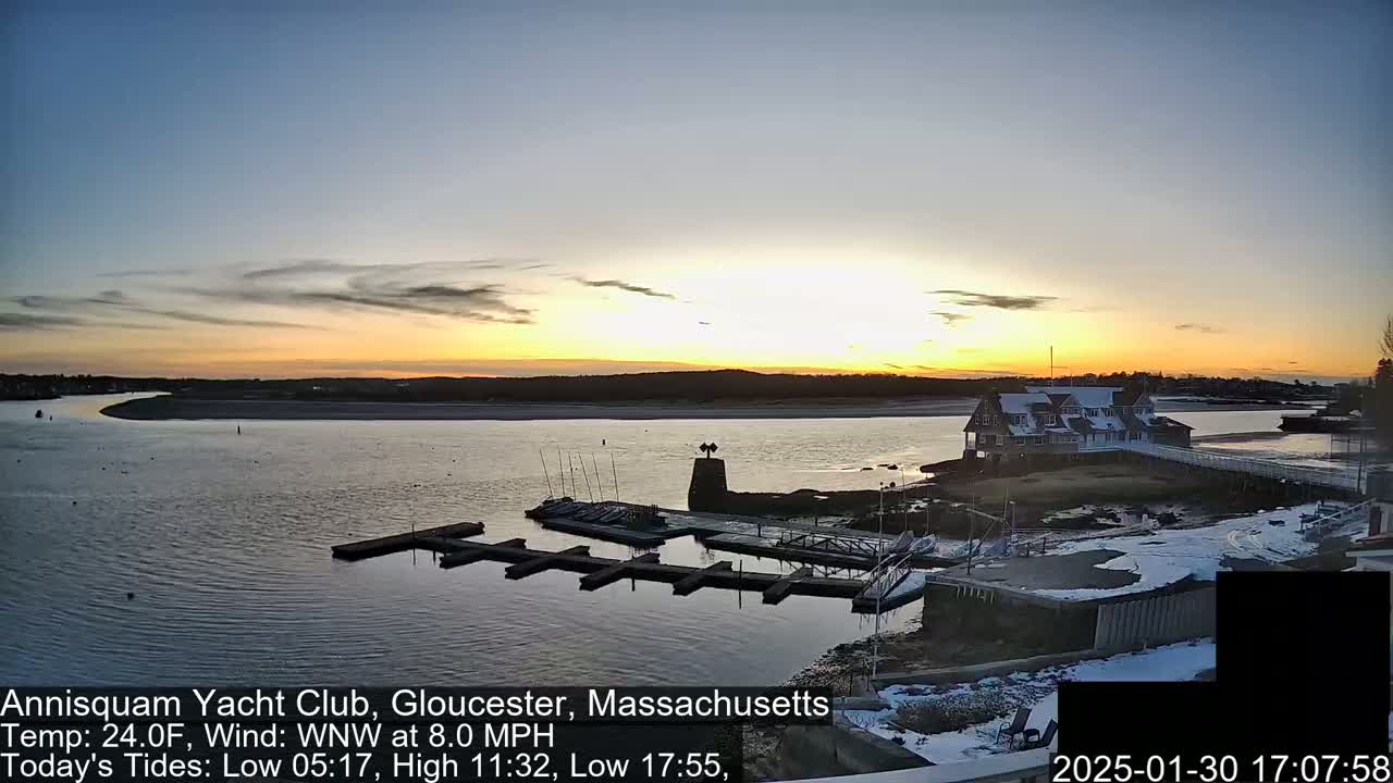A sunset over a calm body of water with a marina and a building on a small island, some snow is visible on the ground.