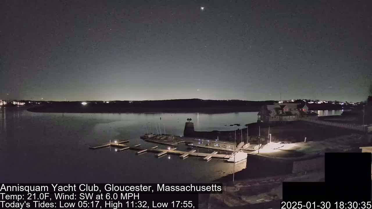 A nighttime view of a calm body of water with docked boats and a building, under a clear, dark sky.