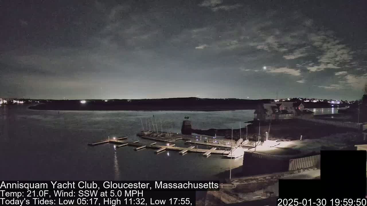 A nighttime view of a marina with docked sailboats under a partly cloudy sky.