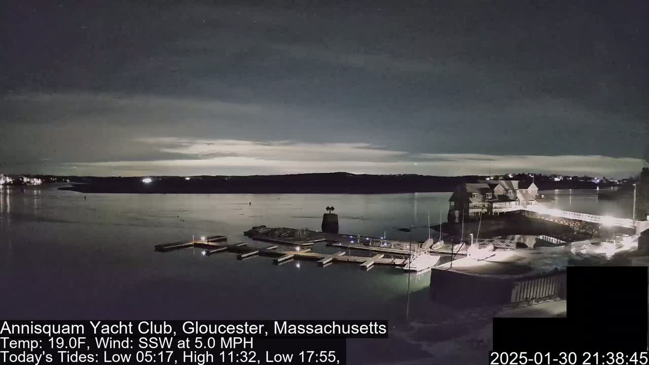 A nighttime view of a marina with docked boats under a partly cloudy sky, and a calm body of water.