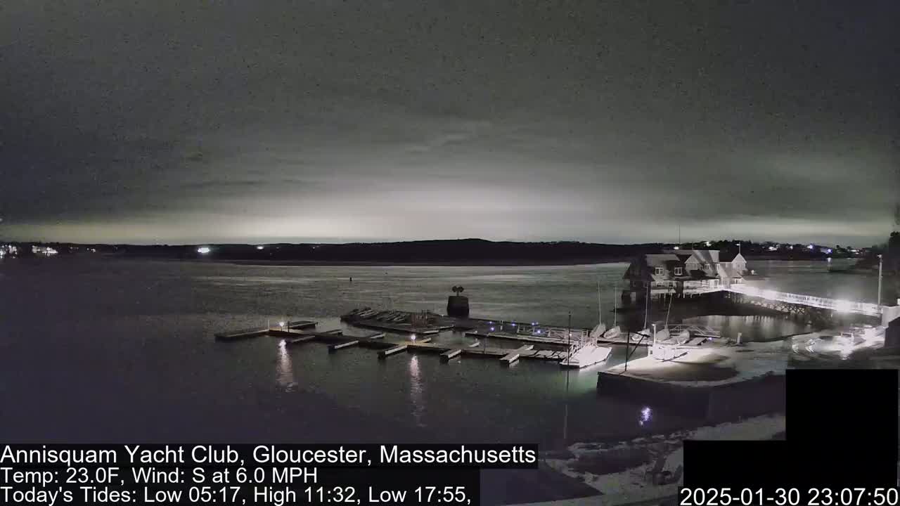A nighttime view of a marina with boats docked, under a dark, cloudy sky.