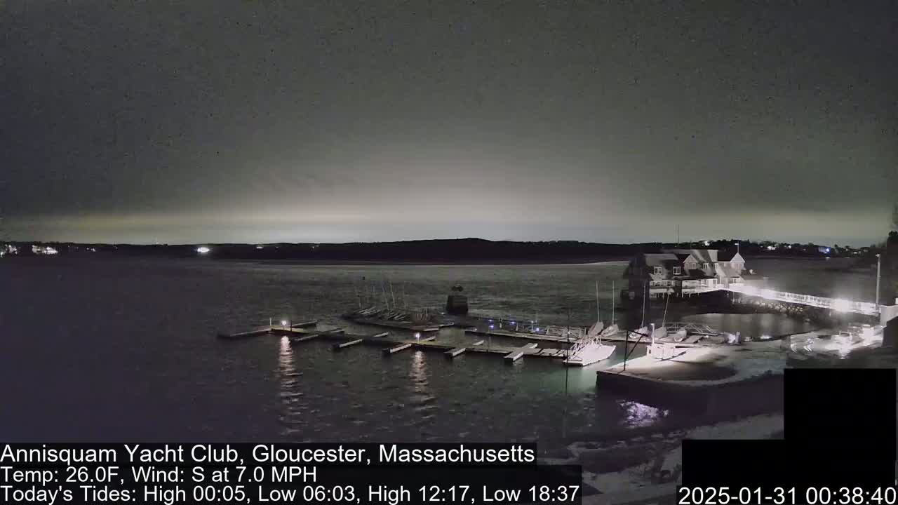 A nighttime view of a marina with boats docked, under a dark, overcast sky.