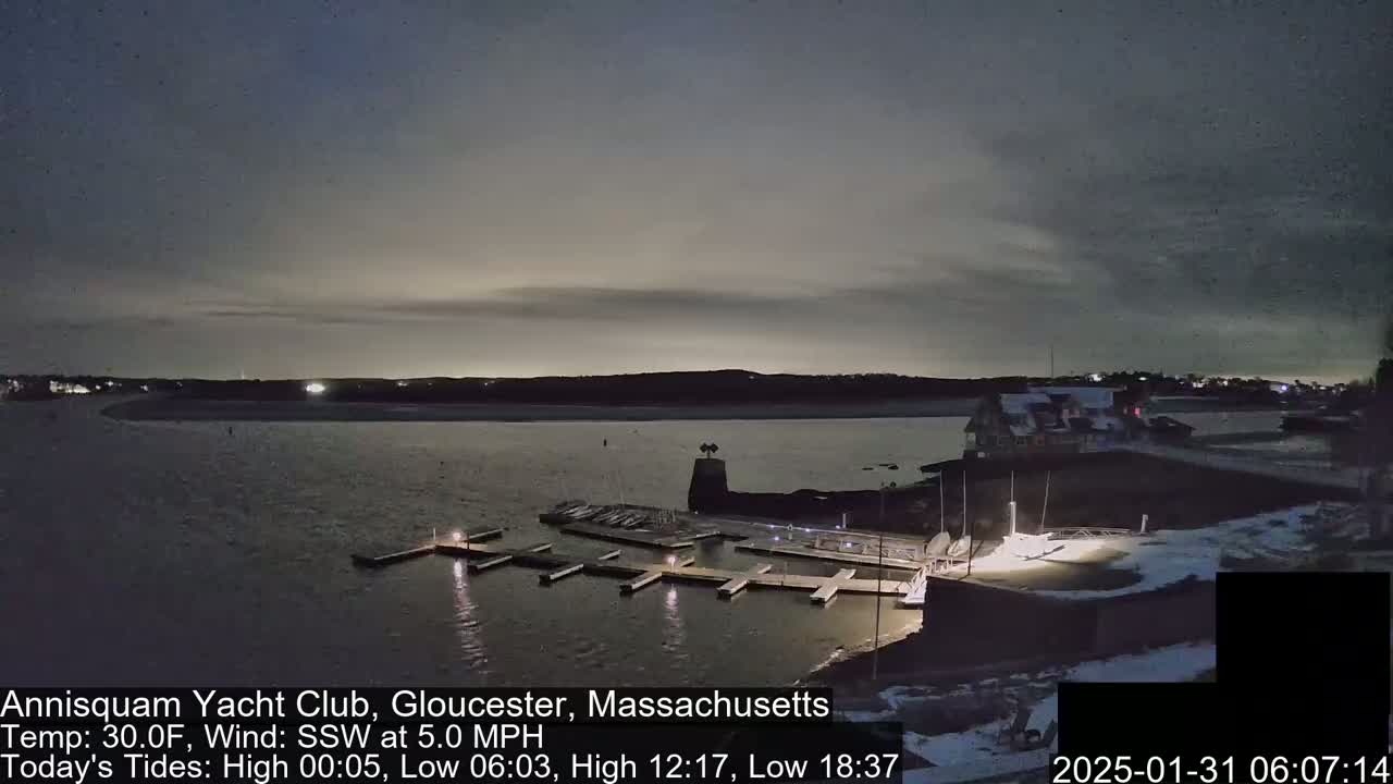 A nighttime view of a snow-dusted marina with docked boats, under a mostly cloudy sky.