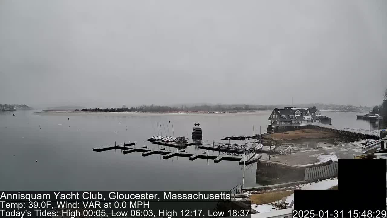 A snow-covered marina with boats docked and a clubhouse is visible on a calm, overcast day.