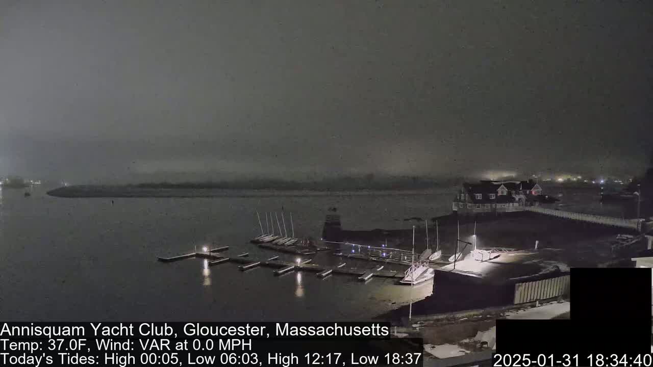 A nighttime, foggy view of a marina with docked sailboats and a clubhouse under a dark sky.