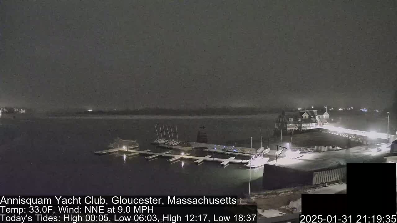 A nighttime view of a yacht club harbor with docked sailboats under a lightly snowing sky.