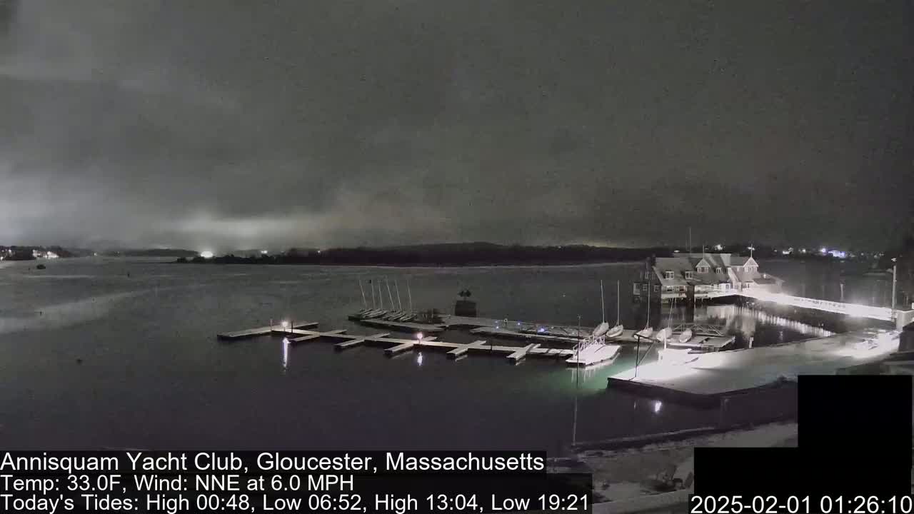 A snow-covered marina with docked sailboats is seen at night under a dark, cloudy sky.