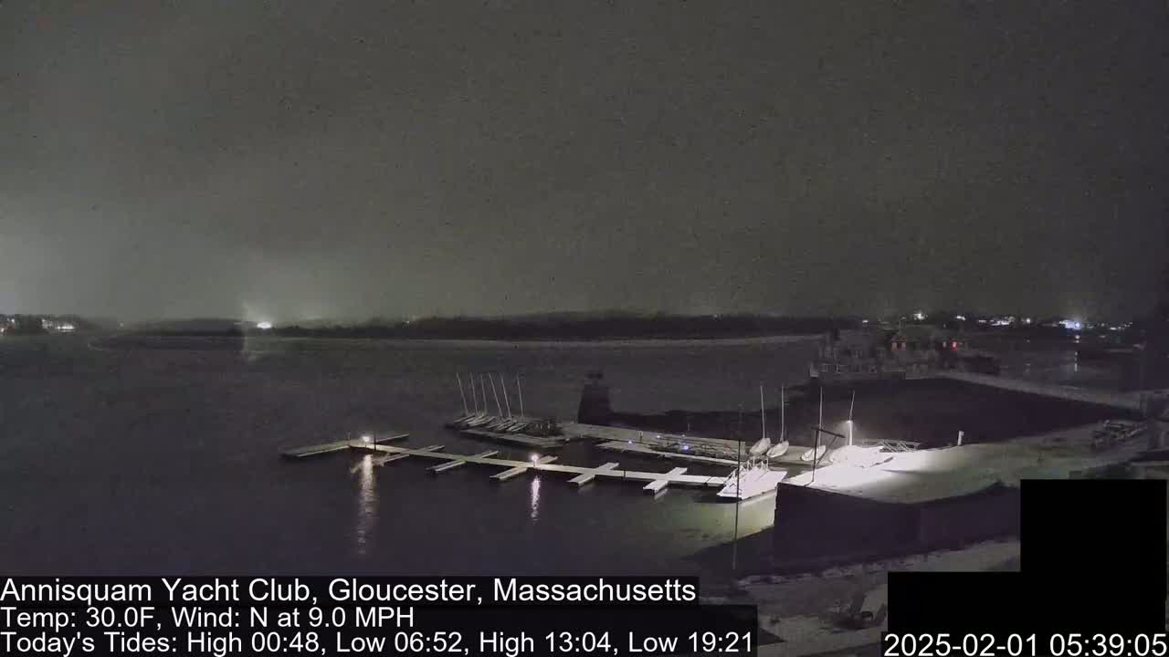 A nighttime, snow-covered marina with boats docked under a dark, lightly snowing sky.