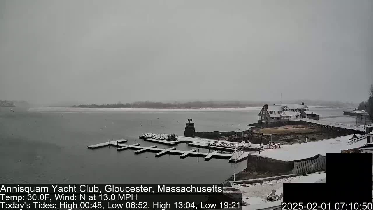 A snow-covered marina with a building in the background during a light snowfall.
