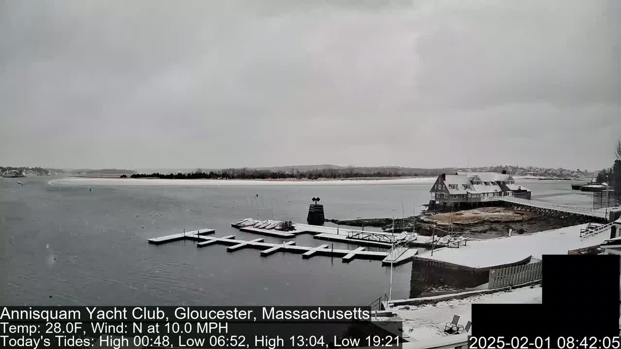 A snow-covered marina with boats docked and a building on a small island, under a gray, overcast sky.