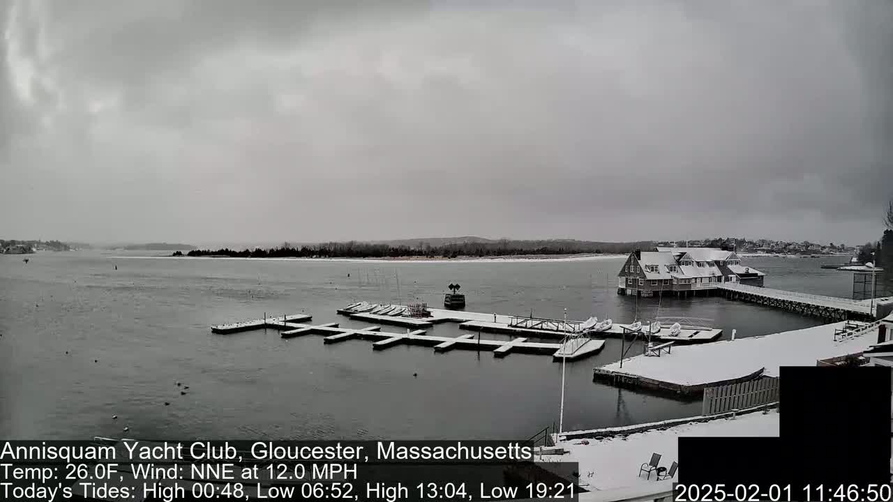 A snow-covered marina with boats docked and a building in the background under an overcast sky.