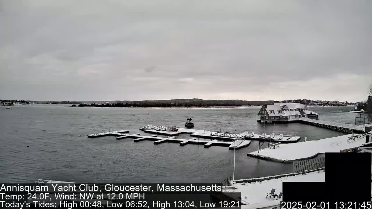 A snow-covered marina with boats docked and a clubhouse, situated on a body of water under an overcast sky.