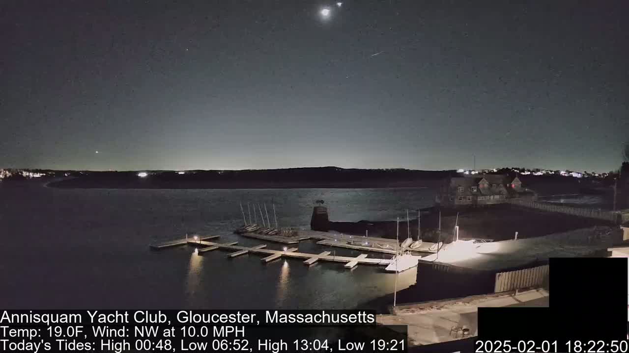 A nighttime view of a marina with boats docked, under a dark sky with a few stars and planets visible, and a 10 mph northwest wind.