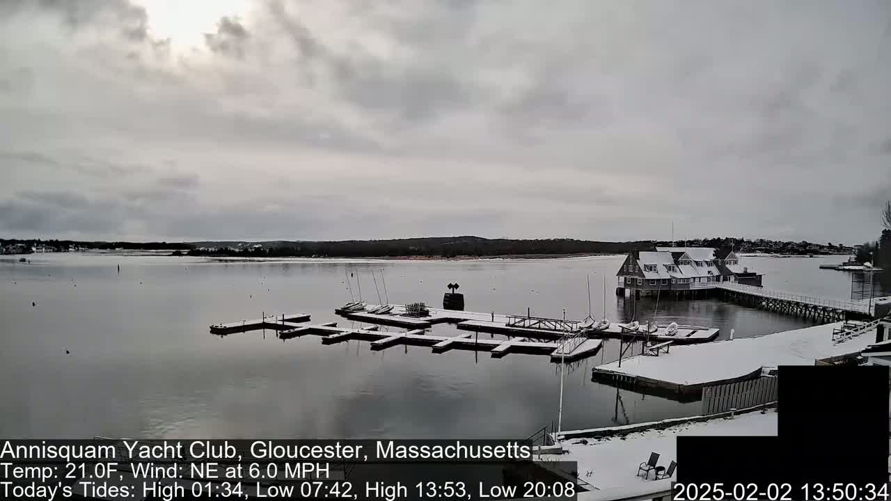 A snow-covered marina with sailboats docked at a clubhouse, under a cloudy sky.