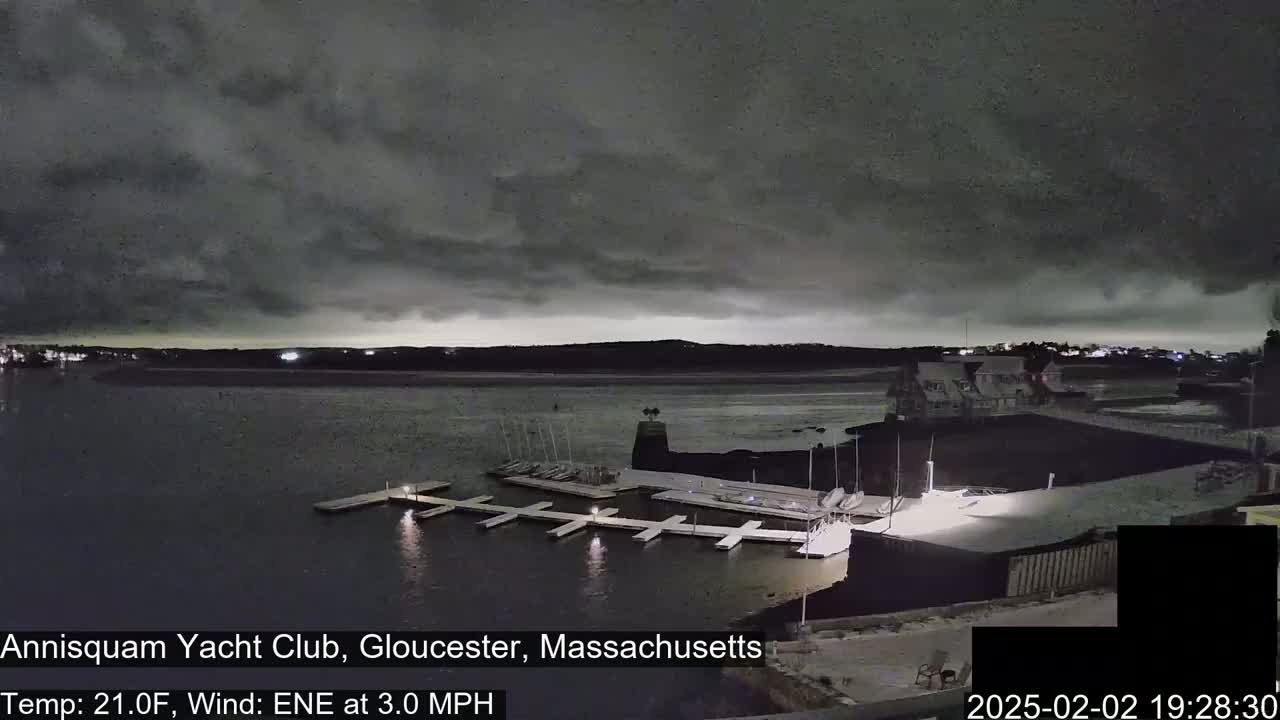 A nighttime view of a marina with docked sailboats under a dark, cloudy sky.