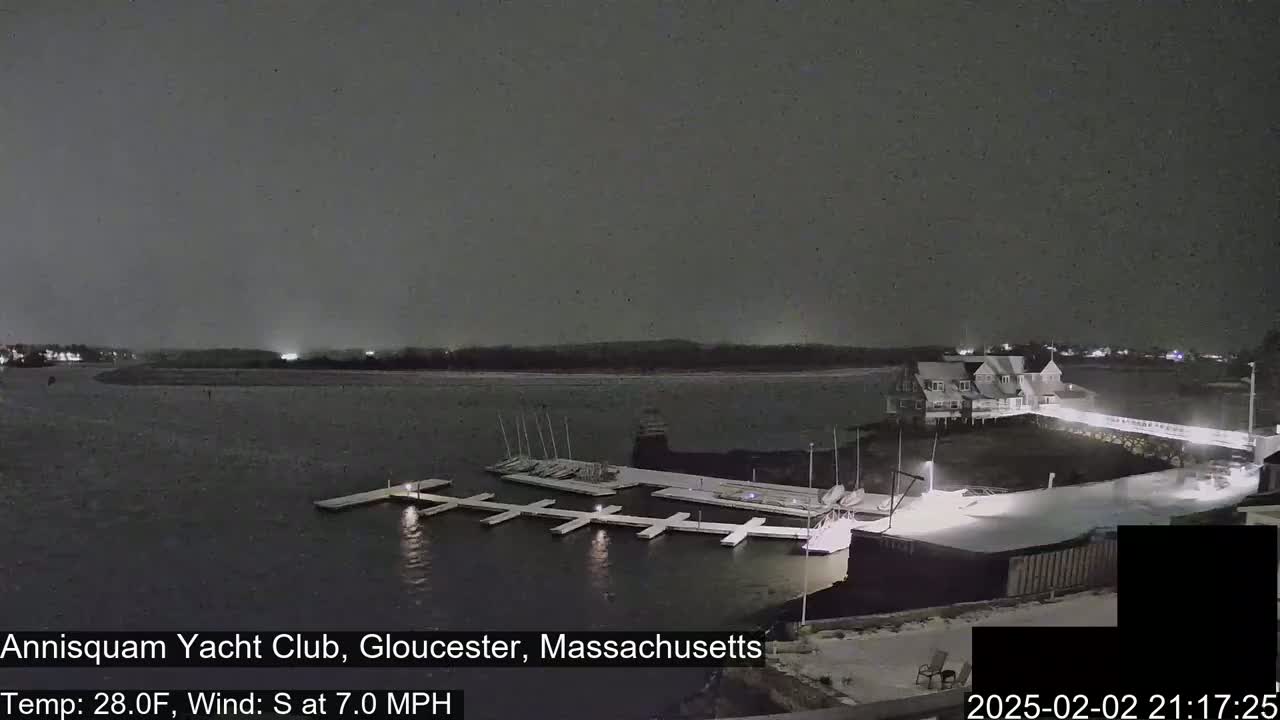 A nighttime view of a snow-covered yacht club marina with boats docked, under a dark, snowy sky.