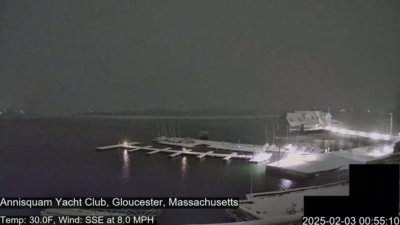 A snow-covered marina with boats docked at night during a snowfall.
