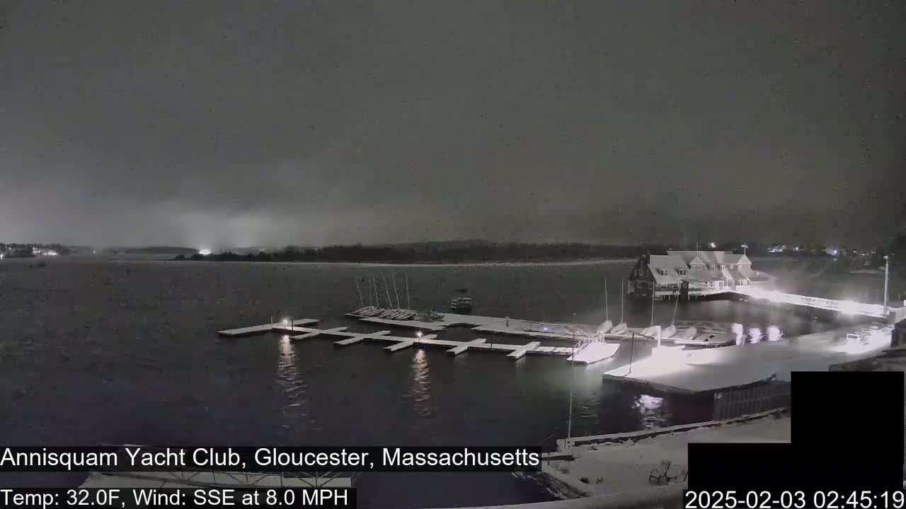 A snow-covered marina with boats docked at night during a light snowfall.