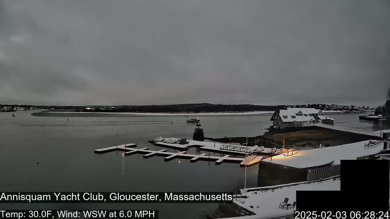 A snow-covered marina with a building and several boats is visible under a gray sky, with a light wind.