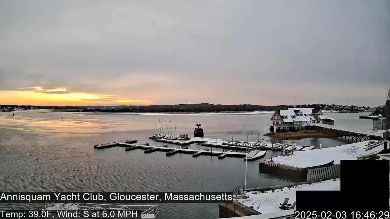 A snow-dusted marina with a clubhouse is seen at sunset under a partly cloudy sky.