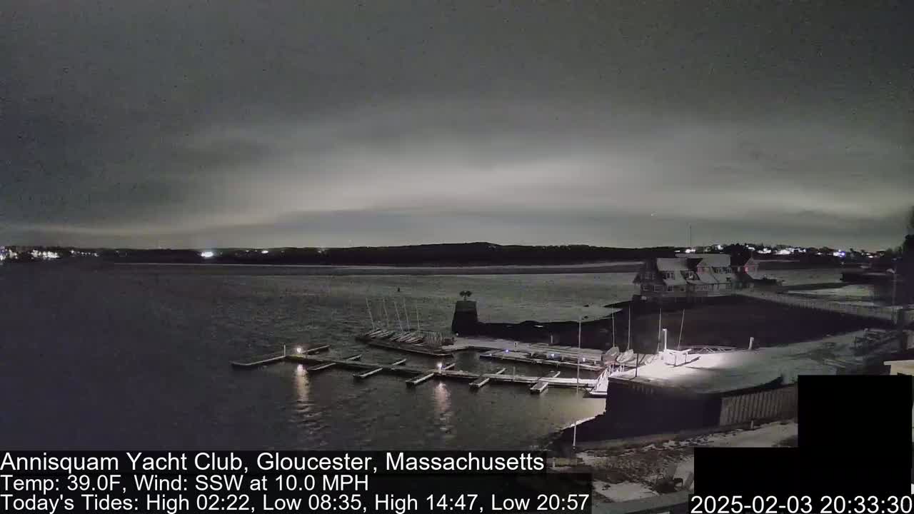 A nighttime view of a marina with boats docked, under a cloudy sky and a 10 mph southwest wind.