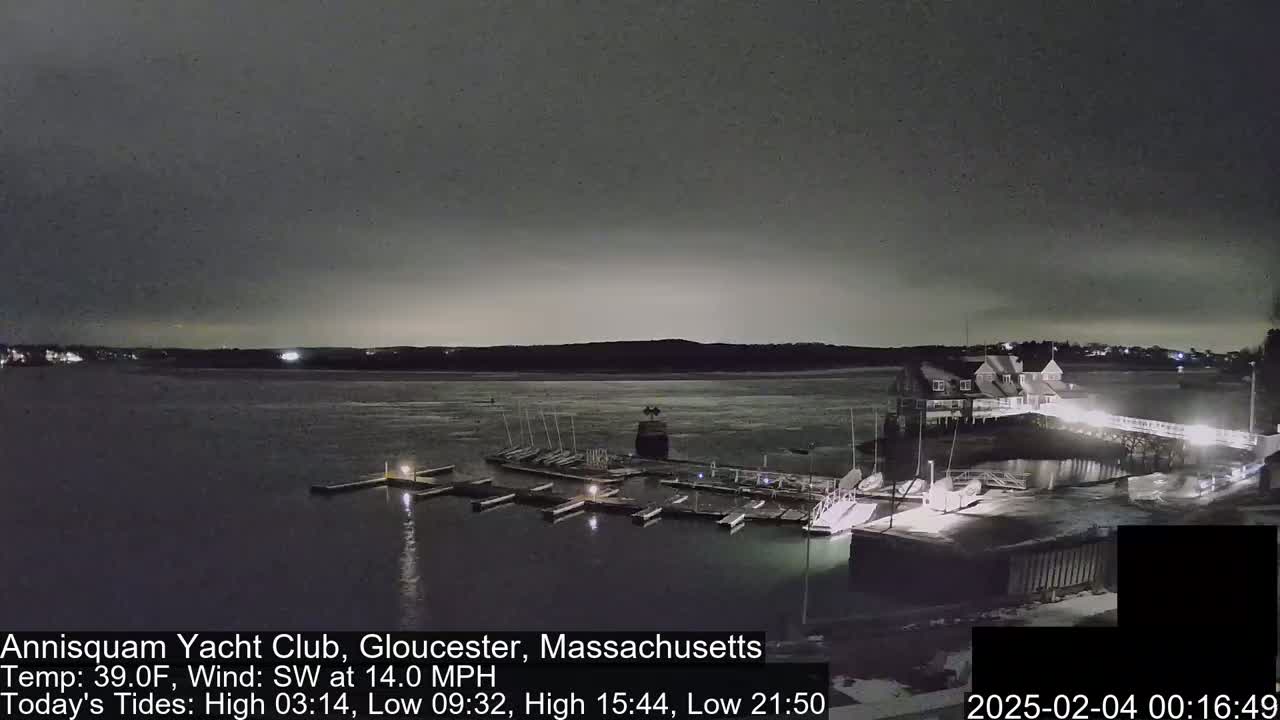 A nighttime view of a yacht club harbor with numerous boats docked under a dark, overcast sky.