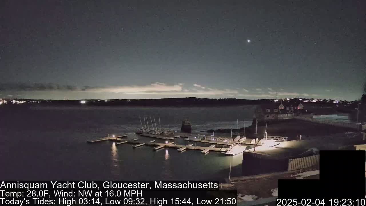 A nighttime view of a marina with sailboats docked, under a mostly clear sky with a northwest wind.